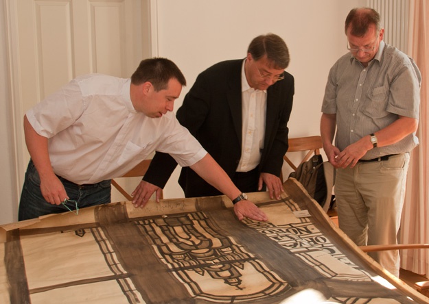 Kaplan Daniel Laske, Pfarrer Wolfgang Křesák und Bauingenieur Dr. Jürgen Heidan (von links) betrachten einen Originalentwurf des Fensters "Pforte des Himmels"